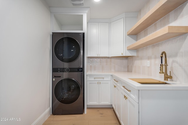 laundry area featuring cabinets, stacked washer and dryer, light hardwood / wood-style floors, and sink