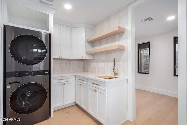 washroom with cabinets, light wood-type flooring, sink, and stacked washer and clothes dryer