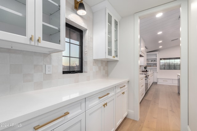 kitchen featuring light wood-type flooring, vaulted ceiling, decorative backsplash, and white cabinetry