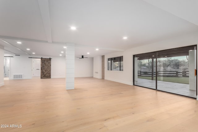 empty room with light wood-type flooring, beam ceiling, and a barn door