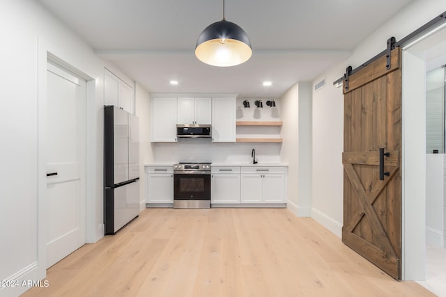 kitchen with light hardwood / wood-style flooring, white cabinetry, appliances with stainless steel finishes, and a barn door