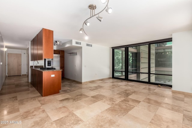 kitchen featuring a wall of windows, brown cabinets, baseboards, dark stone counters, and a sink