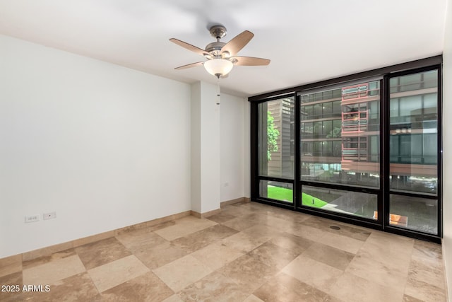 empty room with expansive windows, ceiling fan, and baseboards
