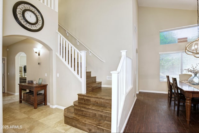 stairs with an inviting chandelier, arched walkways, baseboards, and a towering ceiling