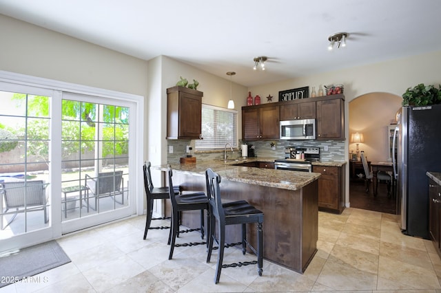 kitchen featuring light stone counters, a breakfast bar, a sink, stainless steel appliances, and decorative backsplash