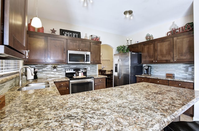 kitchen with appliances with stainless steel finishes, tasteful backsplash, light stone countertops, a sink, and a peninsula