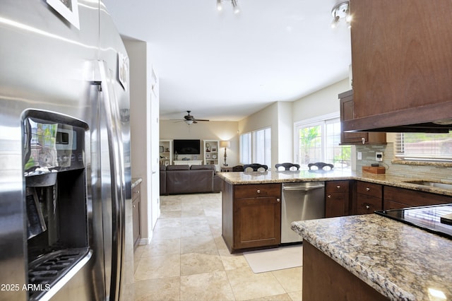 kitchen featuring light stone counters, a peninsula, appliances with stainless steel finishes, and tasteful backsplash