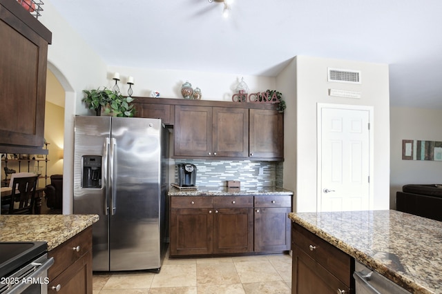 kitchen with light stone countertops, dark brown cabinetry, stainless steel appliances, backsplash, and visible vents