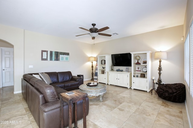 living room featuring visible vents, baseboards, ceiling fan, arched walkways, and light tile patterned floors