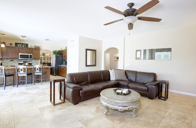 living room with baseboards, arched walkways, a ceiling fan, and light tile patterned floors