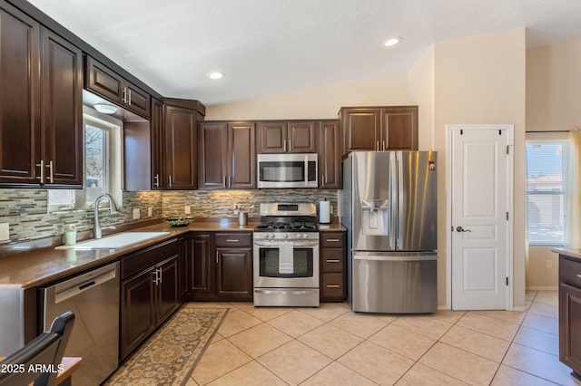 kitchen with light tile patterned floors, lofted ceiling, a sink, dark brown cabinets, and appliances with stainless steel finishes