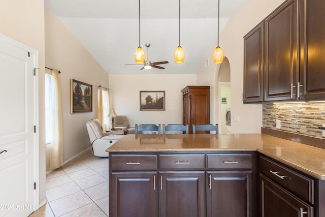 kitchen featuring tasteful backsplash, dark brown cabinetry, a peninsula, light tile patterned flooring, and vaulted ceiling