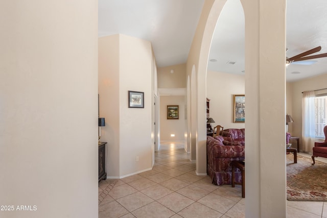 hallway with light tile patterned floors, baseboards, and arched walkways