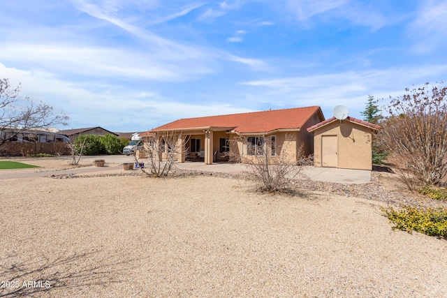 ranch-style house with a tile roof, stucco siding, an outbuilding, a storage unit, and a patio