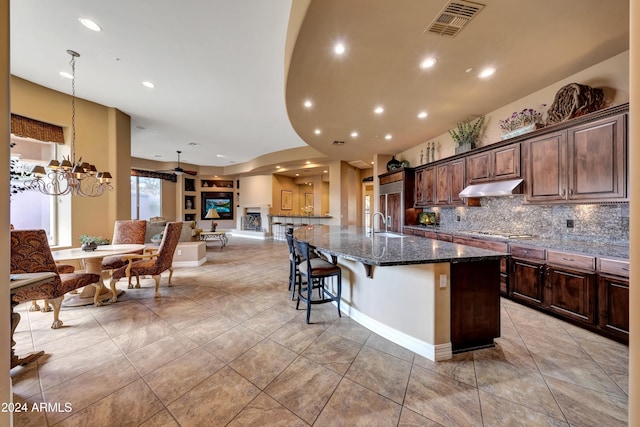 kitchen with a kitchen breakfast bar, dark stone counters, gas stovetop, an inviting chandelier, and a large island