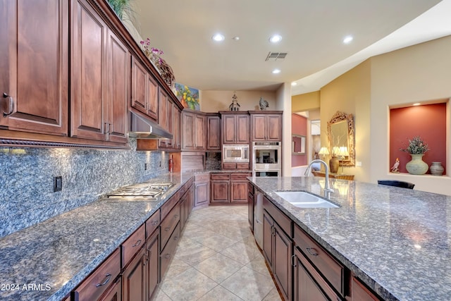 kitchen with sink, backsplash, dark stone countertops, light tile patterned flooring, and appliances with stainless steel finishes