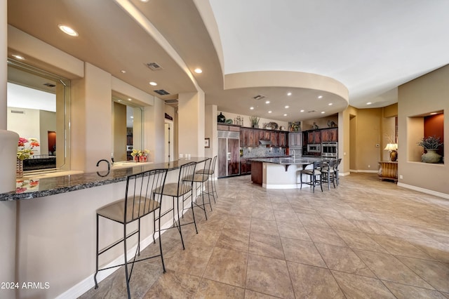 kitchen with decorative backsplash, dark stone countertops, a kitchen bar, kitchen peninsula, and stainless steel appliances