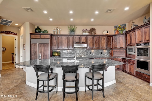 kitchen featuring built in appliances, a large island, dark stone countertops, and sink