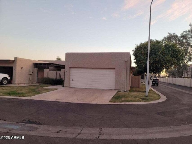 view of front facade featuring fence, an attached garage, stucco siding, and concrete driveway