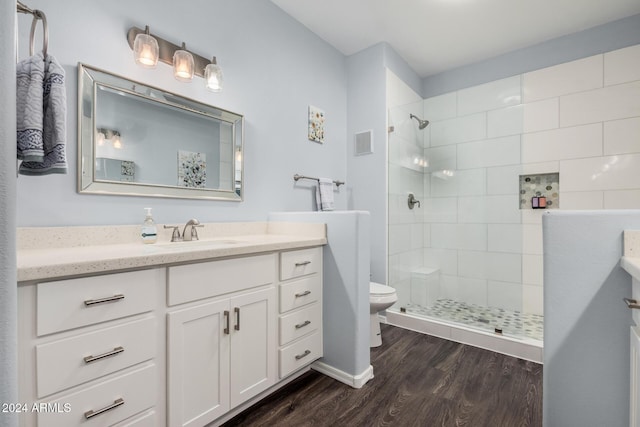 bathroom with a tile shower, hardwood / wood-style floors, vanity, and toilet