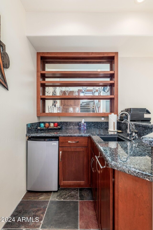 bar featuring dishwasher, dark stone counters, and sink