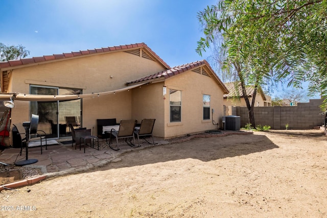 rear view of property featuring central air condition unit, fence, a tiled roof, stucco siding, and a patio area