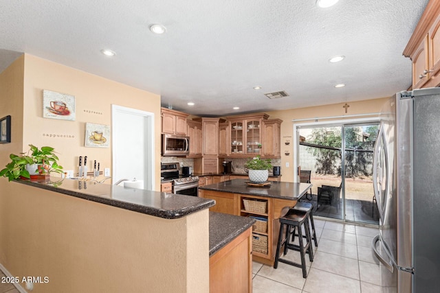 kitchen with light tile patterned flooring, stainless steel appliances, a breakfast bar, a kitchen island, and visible vents