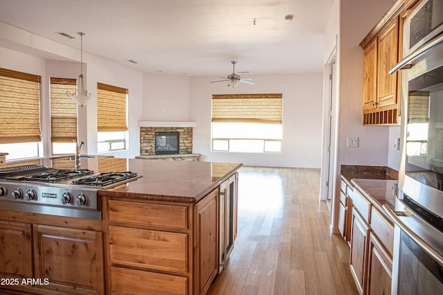 kitchen with brown cabinets, visible vents, appliances with stainless steel finishes, a stone fireplace, and wood finished floors