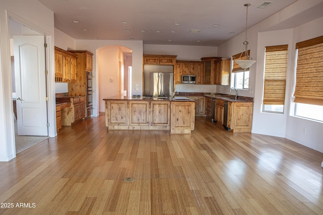 kitchen featuring dark countertops, light wood-style floors, appliances with stainless steel finishes, and arched walkways