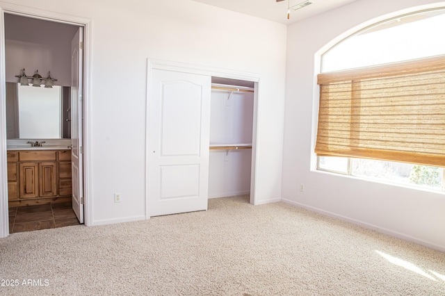 unfurnished bedroom featuring a sink, carpet flooring, baseboards, a closet, and ensuite bath