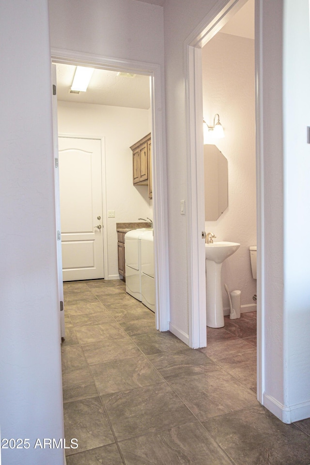 hallway featuring separate washer and dryer, a sink, and baseboards