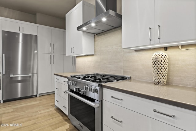 kitchen with backsplash, wall chimney range hood, light hardwood / wood-style flooring, appliances with stainless steel finishes, and white cabinetry