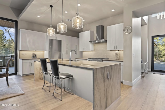 kitchen featuring white cabinets, sink, wall chimney exhaust hood, and a center island with sink