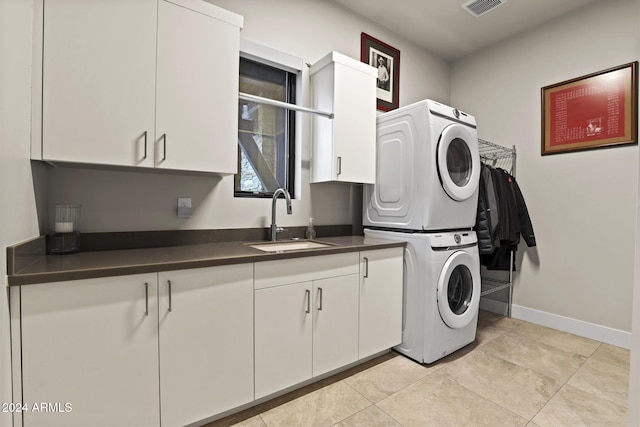 washroom featuring cabinets, light tile patterned floors, stacked washer / drying machine, and sink