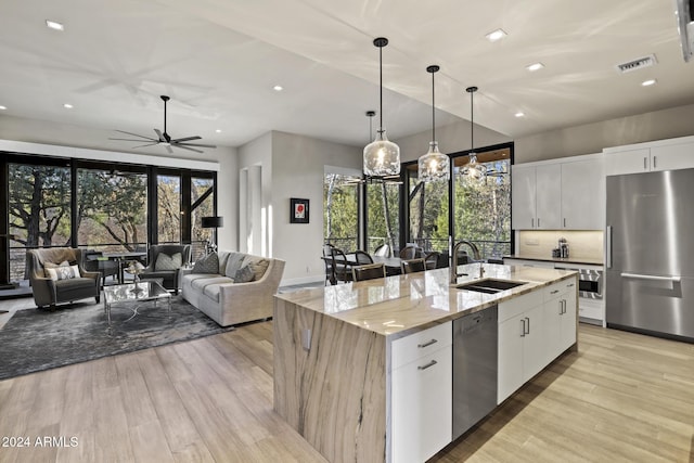 kitchen featuring white cabinets, appliances with stainless steel finishes, light stone countertops, and a kitchen island with sink