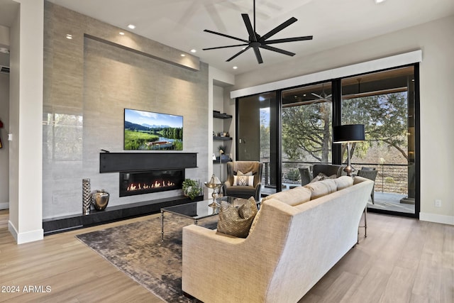 living room featuring ceiling fan, a large fireplace, and light wood-type flooring