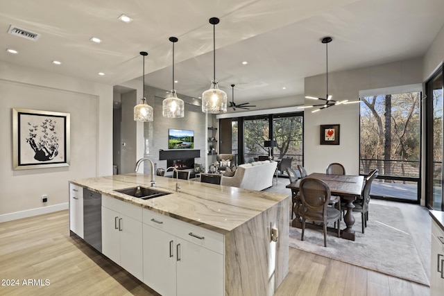 kitchen featuring a center island with sink, sink, ceiling fan, light stone counters, and white cabinetry