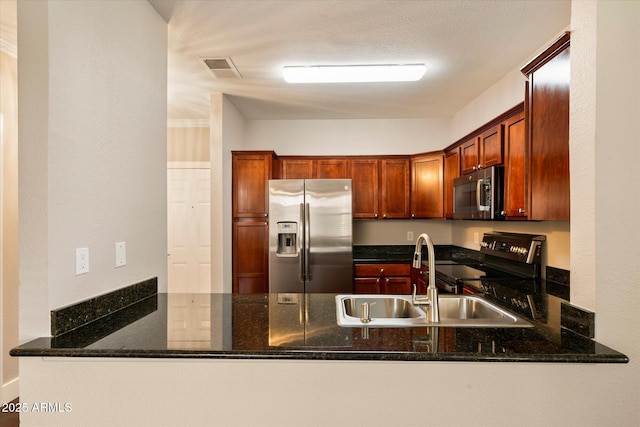 kitchen featuring stainless steel appliances, dark stone counters, a sink, and a peninsula