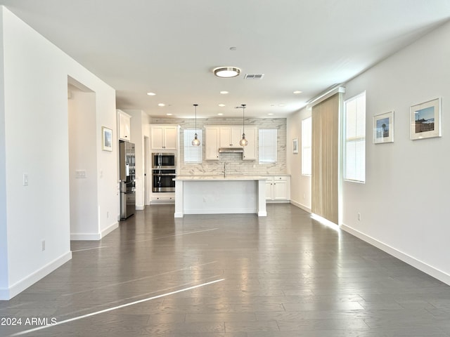 kitchen featuring dark wood-type flooring, white cabinets, an island with sink, backsplash, and decorative light fixtures