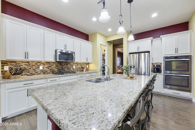 kitchen with a breakfast bar area, tasteful backsplash, appliances with stainless steel finishes, white cabinets, and a sink