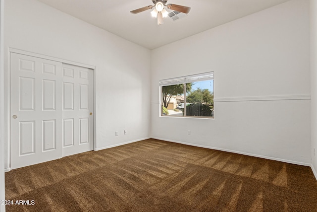 unfurnished bedroom with dark colored carpet, ceiling fan, and a closet