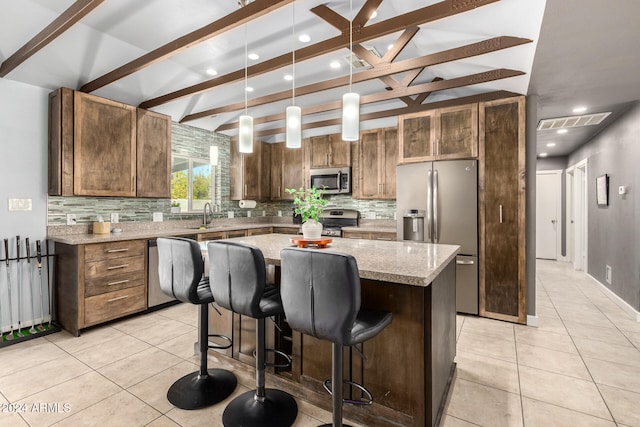 kitchen with light stone counters, stainless steel appliances, a center island, decorative light fixtures, and sink