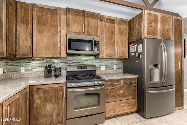 kitchen featuring backsplash, light tile patterned flooring, light stone countertops, and stainless steel appliances