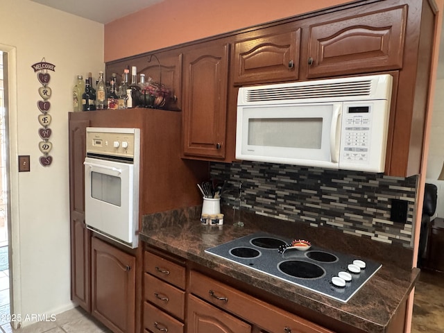 kitchen with brown cabinets, white appliances, decorative backsplash, and dark stone countertops
