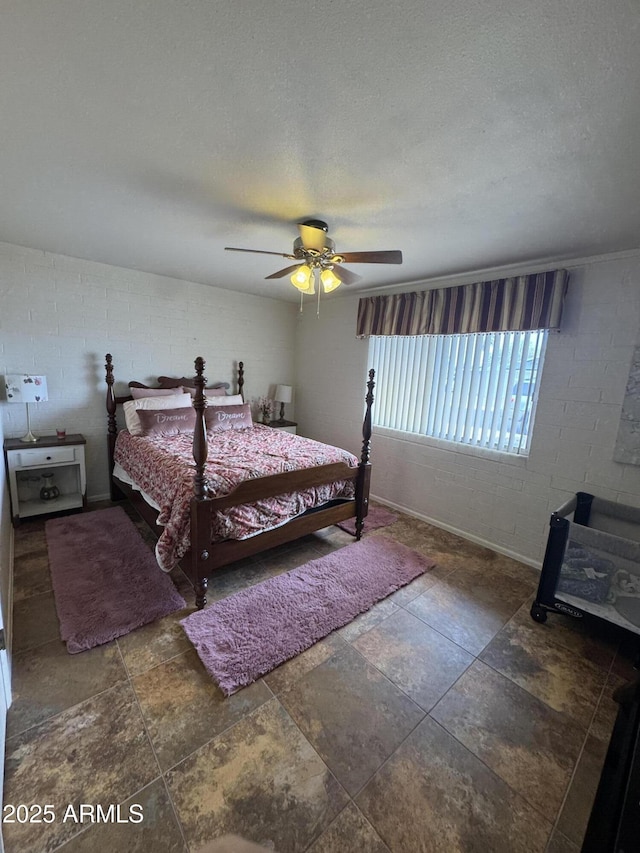 bedroom featuring concrete block wall, stone finish flooring, a ceiling fan, and a textured ceiling