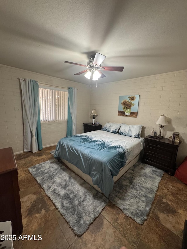 bedroom featuring a textured ceiling, a ceiling fan, and concrete block wall