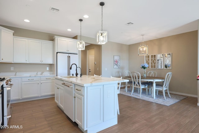 kitchen with sink, white appliances, white cabinetry, a kitchen island with sink, and decorative light fixtures