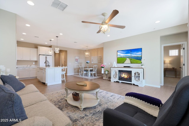 living room featuring ceiling fan, sink, and light hardwood / wood-style floors