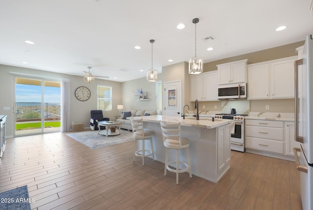 kitchen with pendant lighting, high quality appliances, white cabinetry, an island with sink, and a kitchen bar