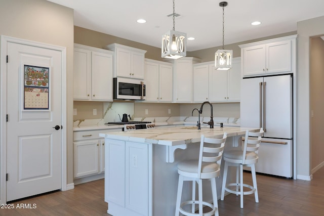 kitchen featuring high end white fridge, white cabinets, and a center island with sink